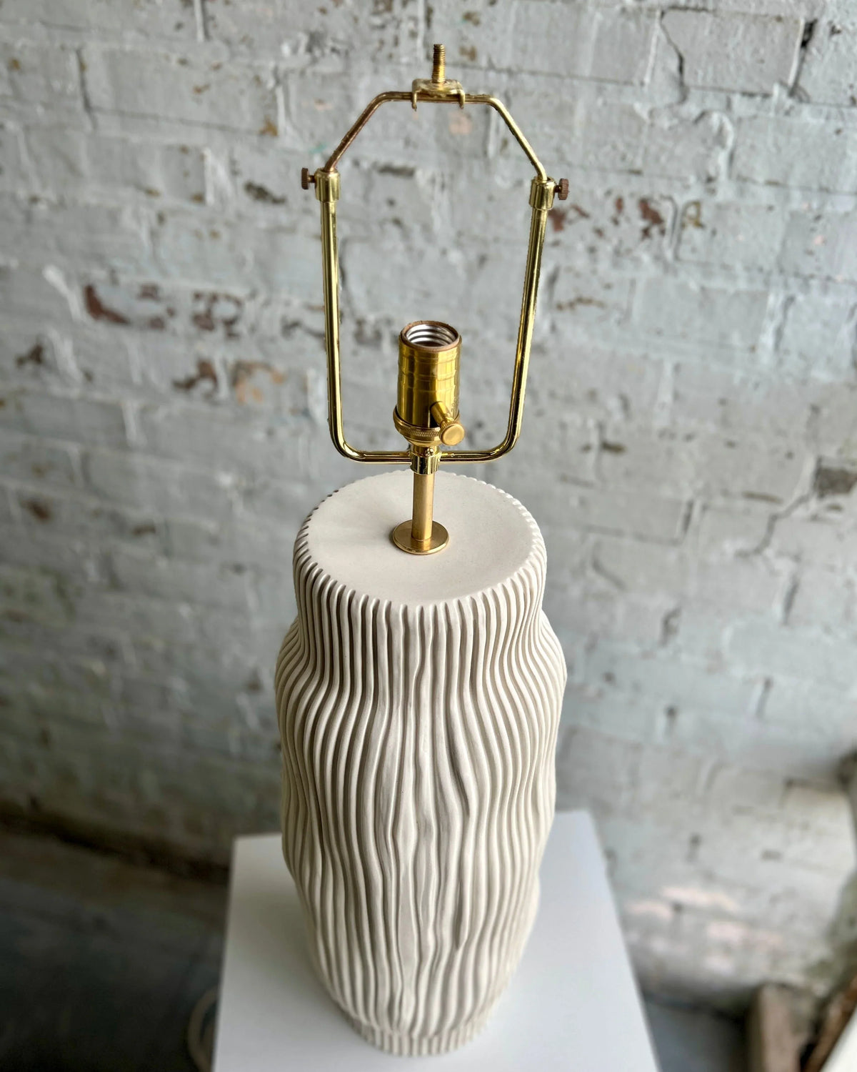 Della table lamp base featuring unglazed cream porcelain and brass hardware, showcasing a textured design.