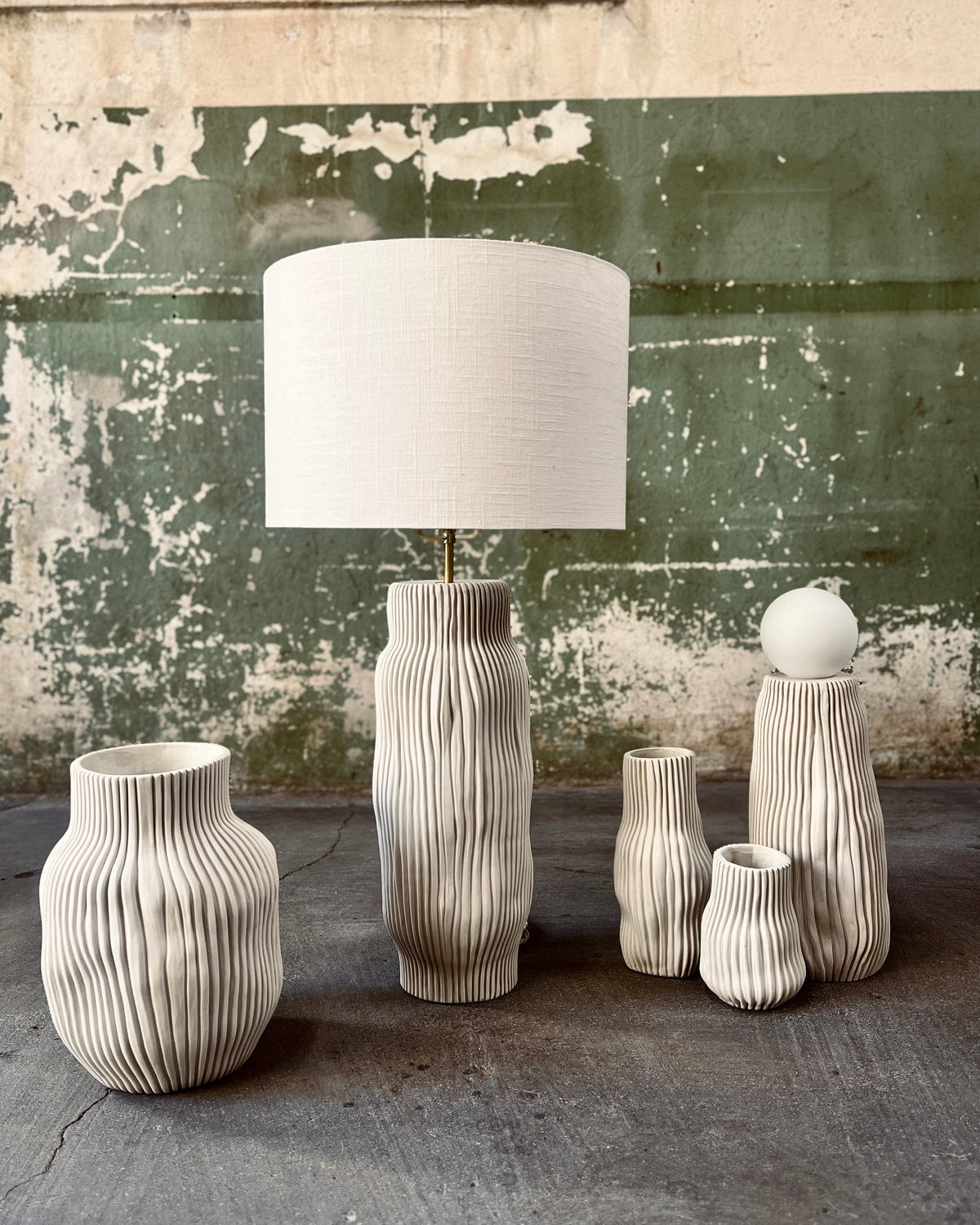 Della table lamp with textured cream porcelain base and off-white linen shade, surrounded by matching vases