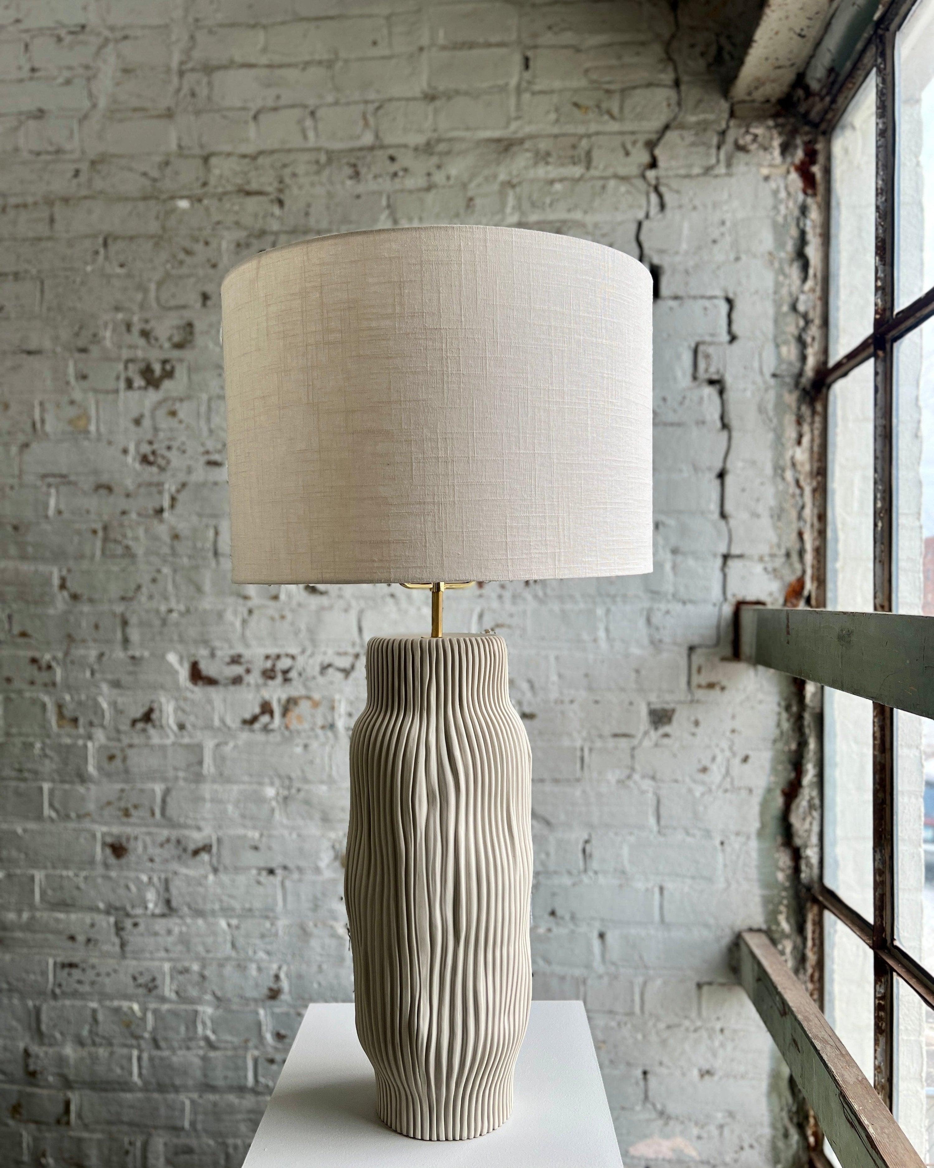 Table lamp with textured base and linen shade.