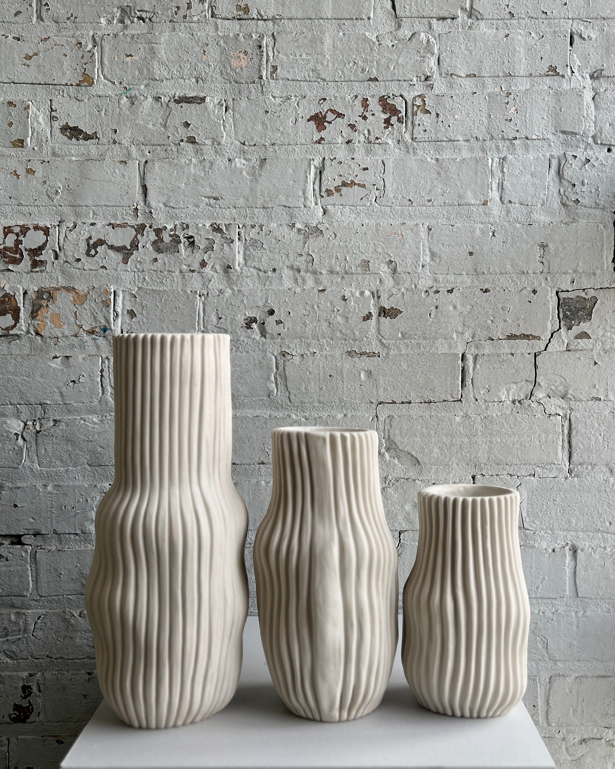 Three textured, beige vases on a white surface.