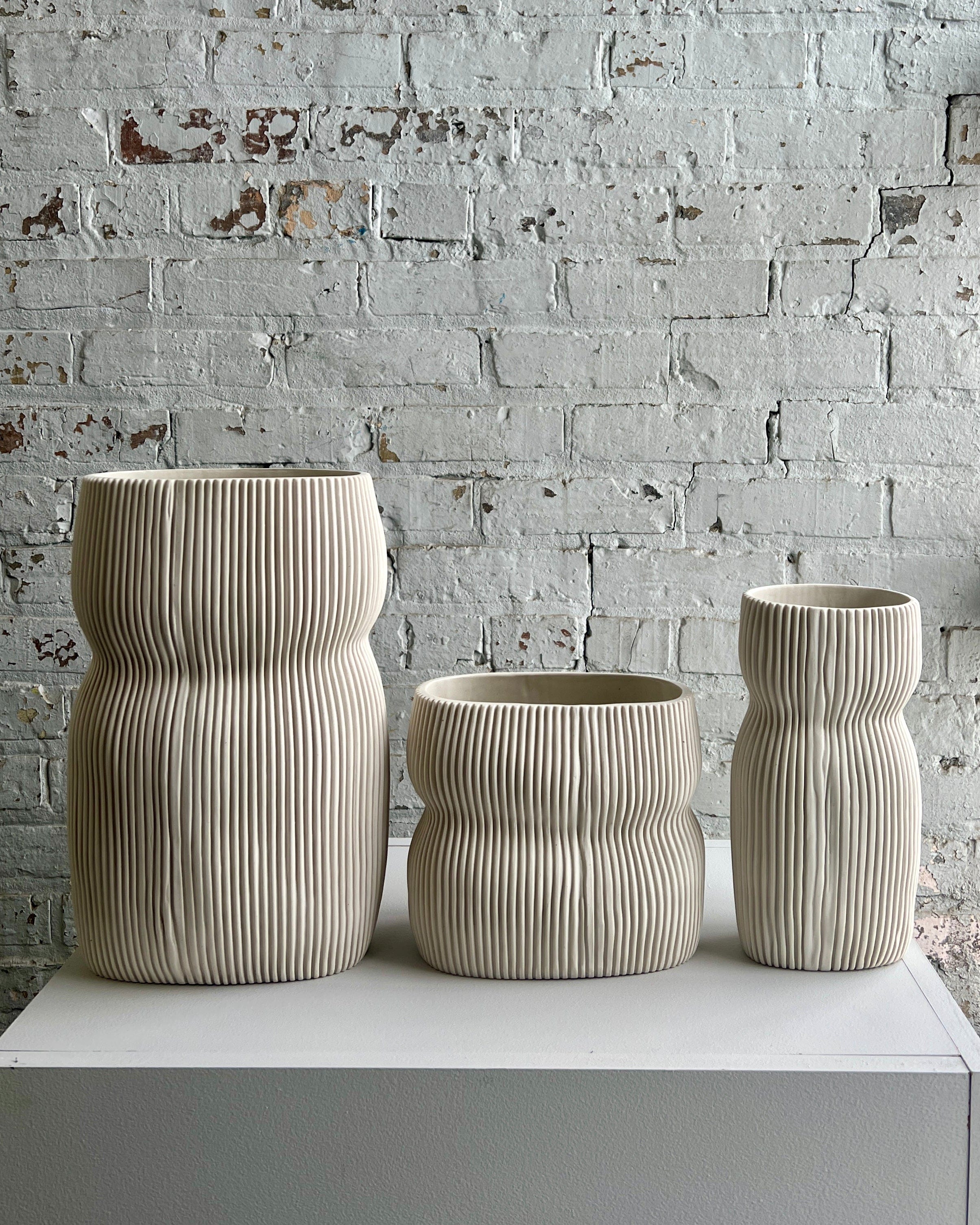 Three beige ribbed vases on a white surface.