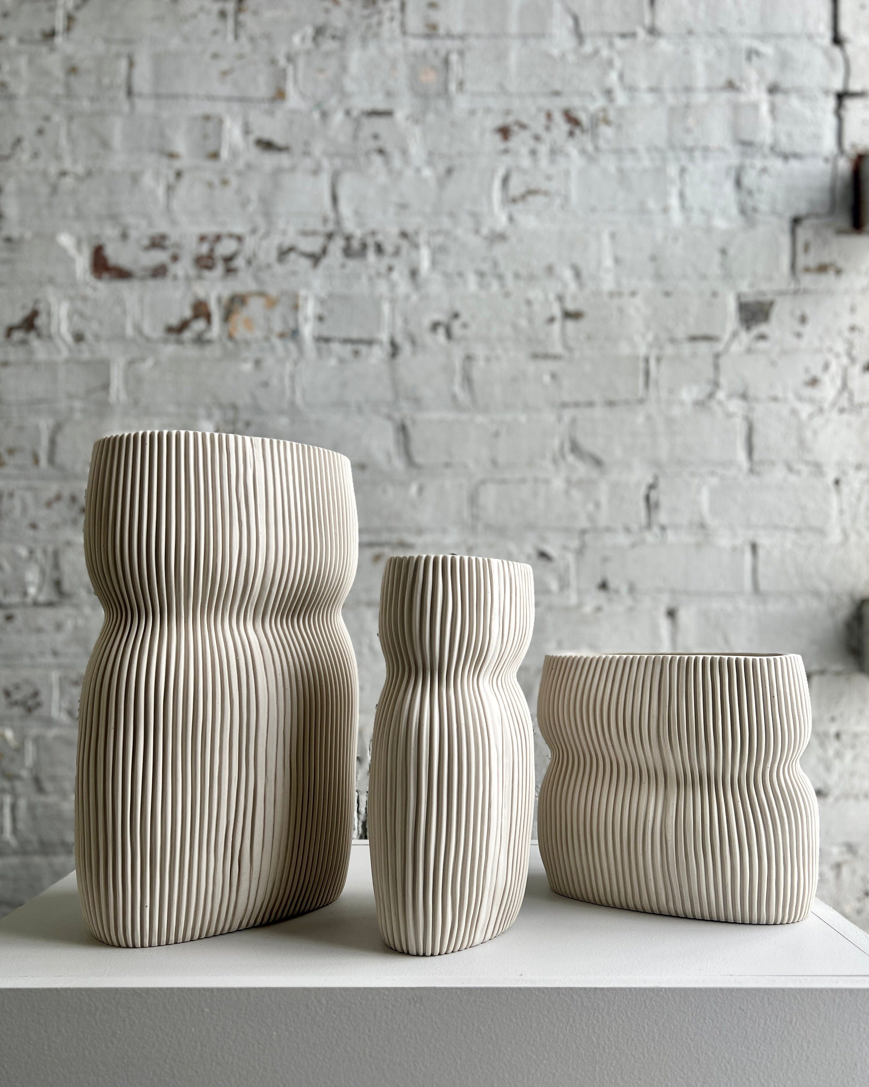 Three ribbed ceramic vases on a white surface.
