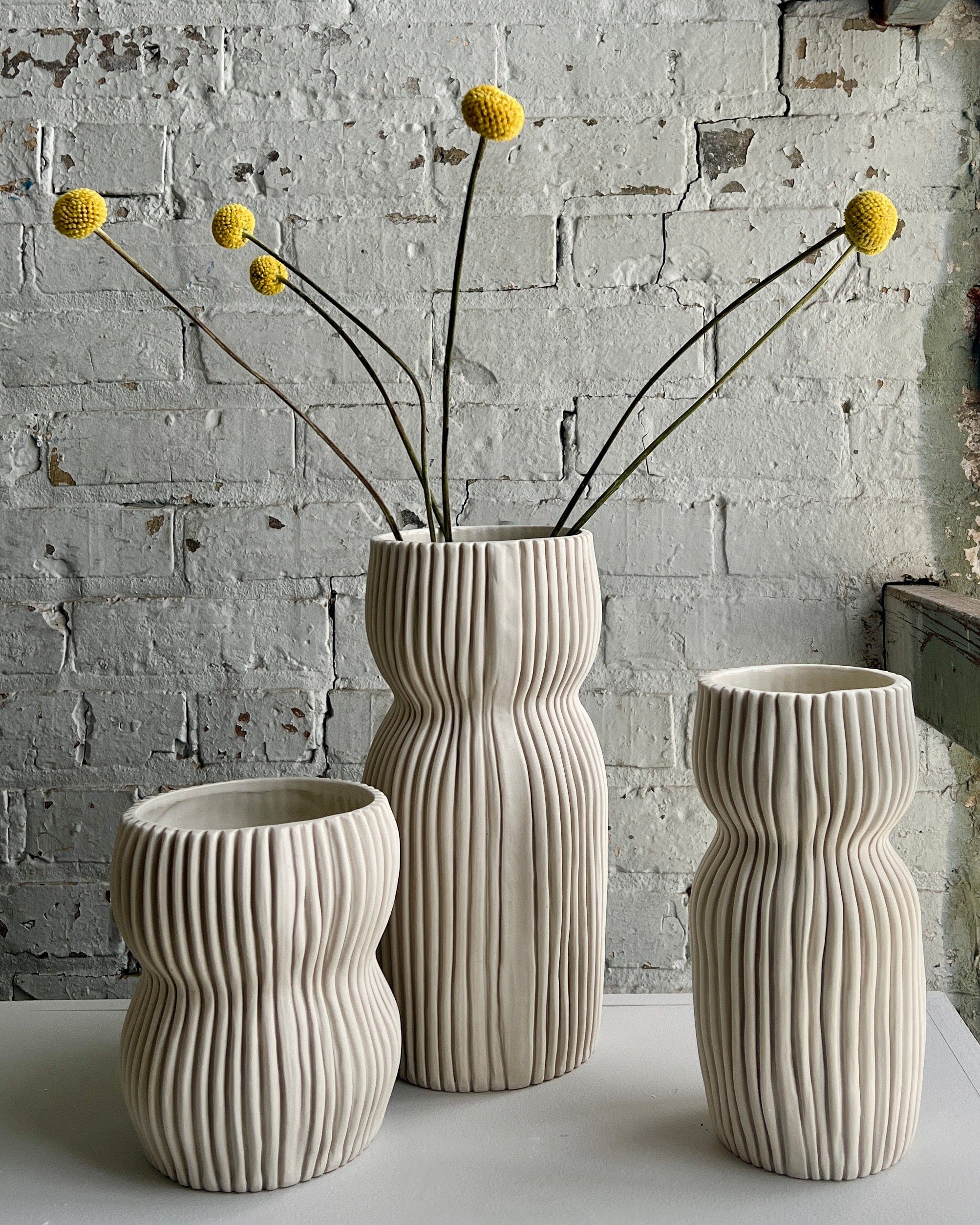 Three textured vases with yellow flowers.