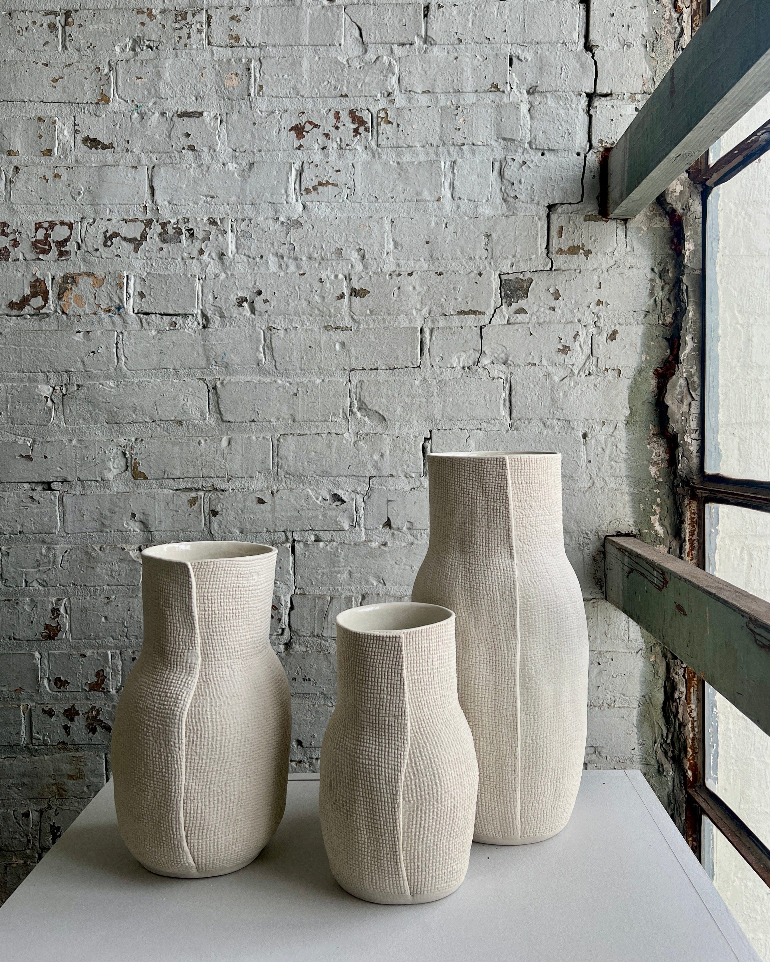 Three cream-colored vases on a white surface.