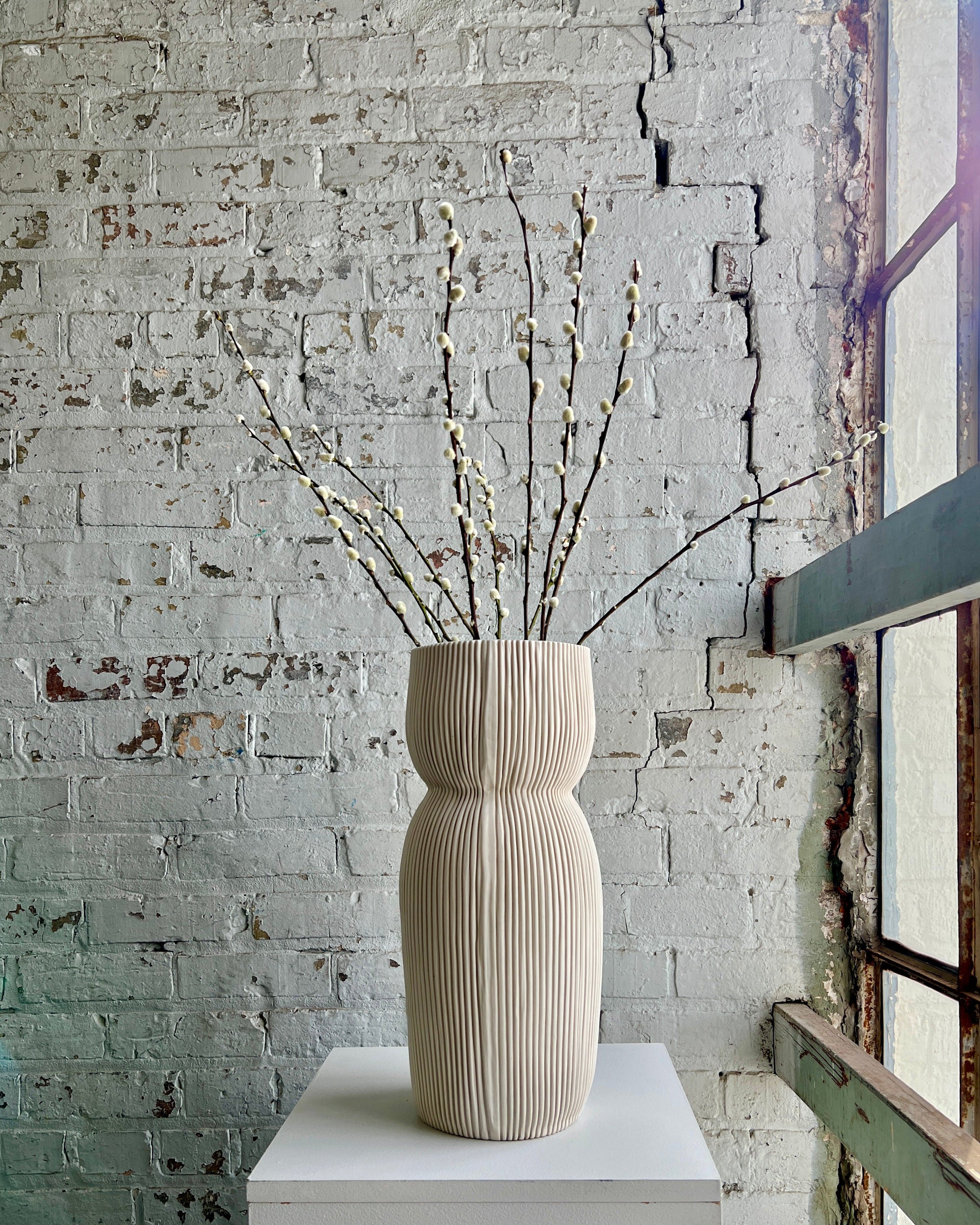 Vase of pussy willow branches on a white stand.