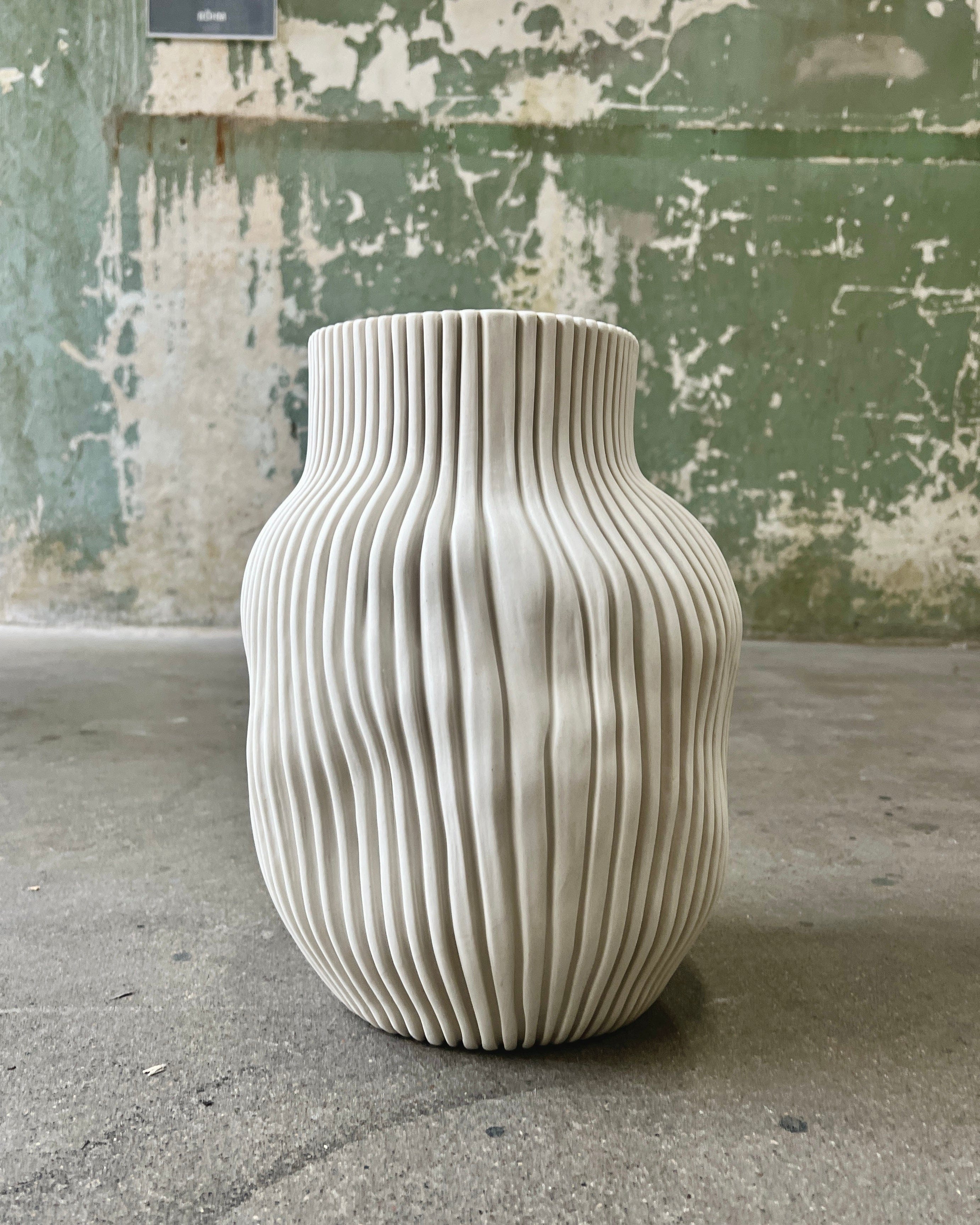 White, textured vase against a mottled green wall.