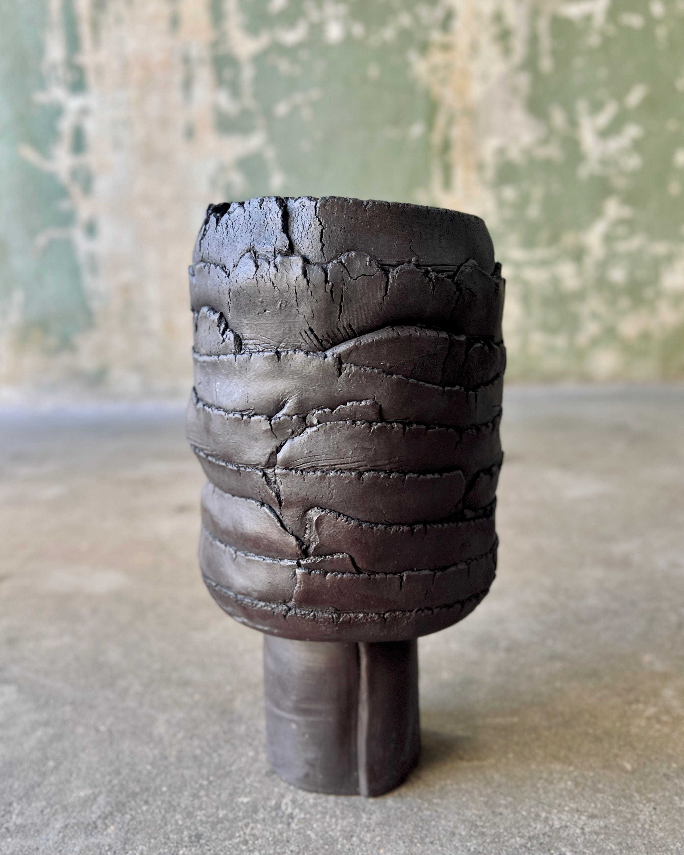 Dark, textured ceramic vase on a pedestal.